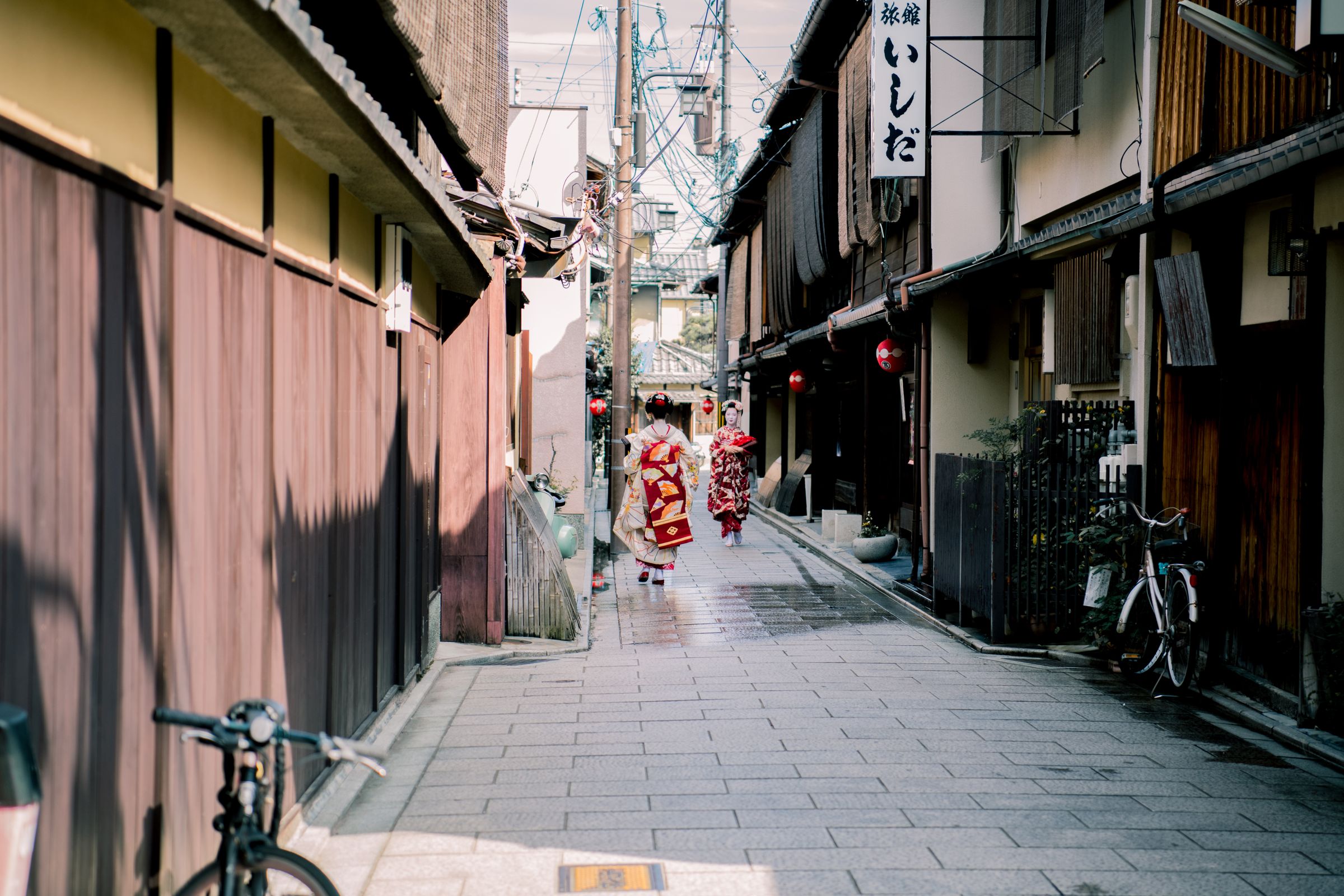 Geishas in traditional attire walking down a historic street in Kyoto, Japan.